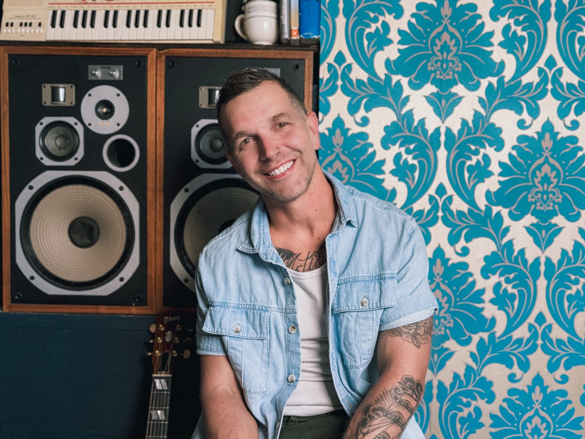 Justin Huey smiling beside vintage speakers and a guitar